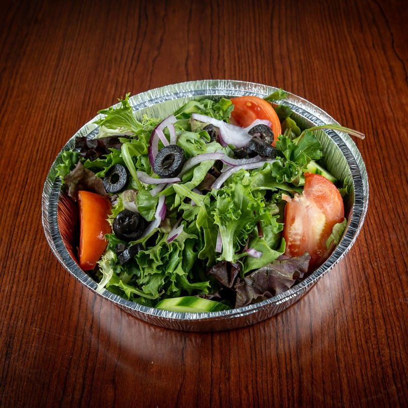 A fresh garden salad with lettuce, tomatoes, black olives, and red onions in a foil container.