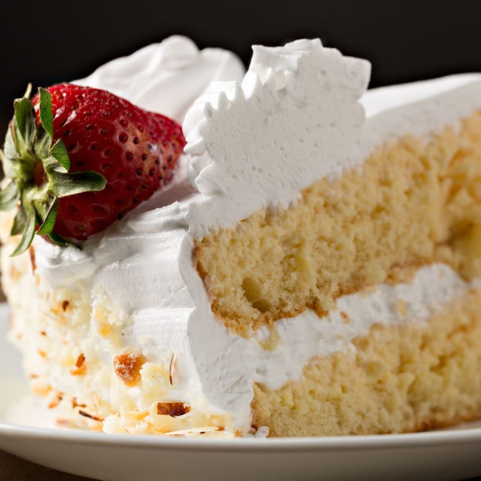 Slice of vanilla cake with white frosting and a fresh strawberry on top.