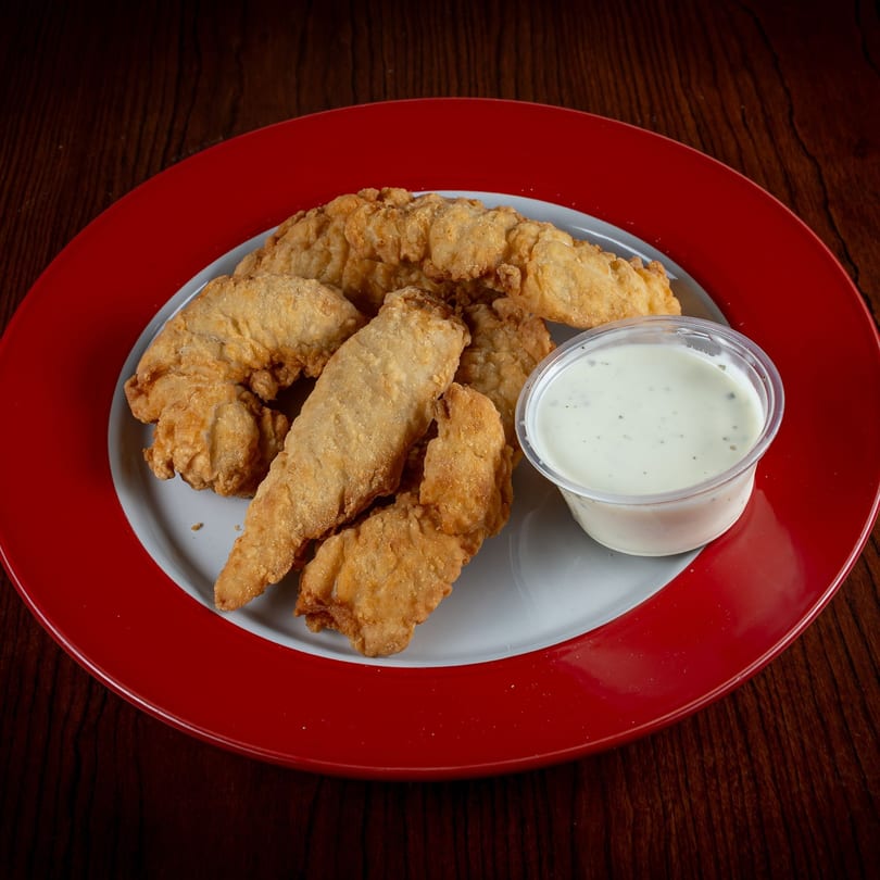Golden-brown chicken tenders and a cup of creamy dipping sauce on a red and white plate.