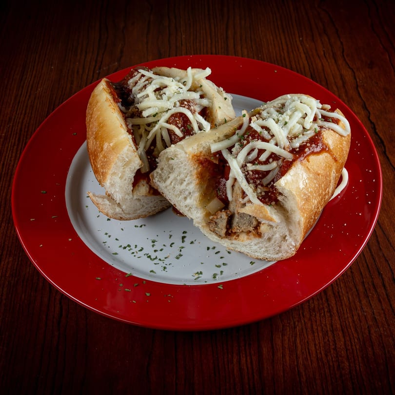 Two halves of a meatball sub with marinara sauce and shredded cheese on a red and white plate.