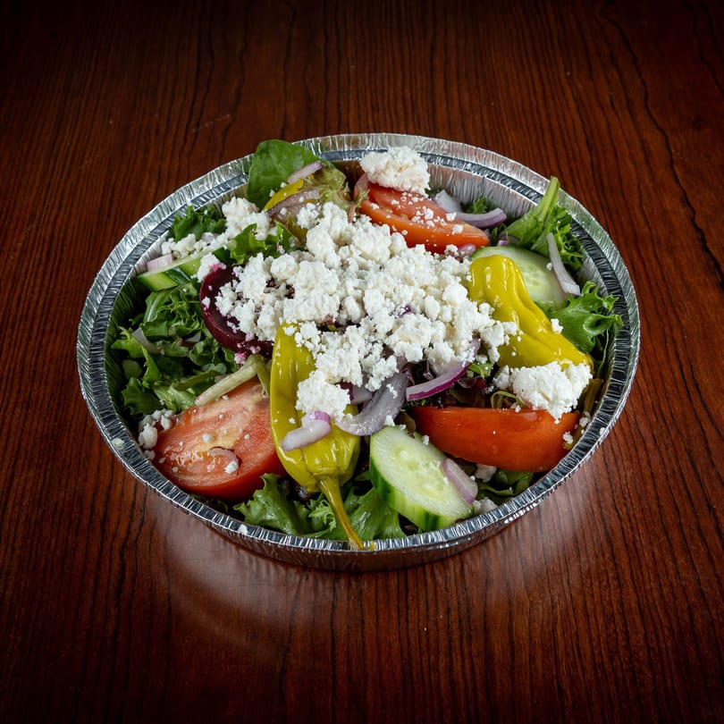 A fresh GoGo Pizza salad with lettuce, tomatoes, cucumbers, peppers, and feta cheese in a foil container.